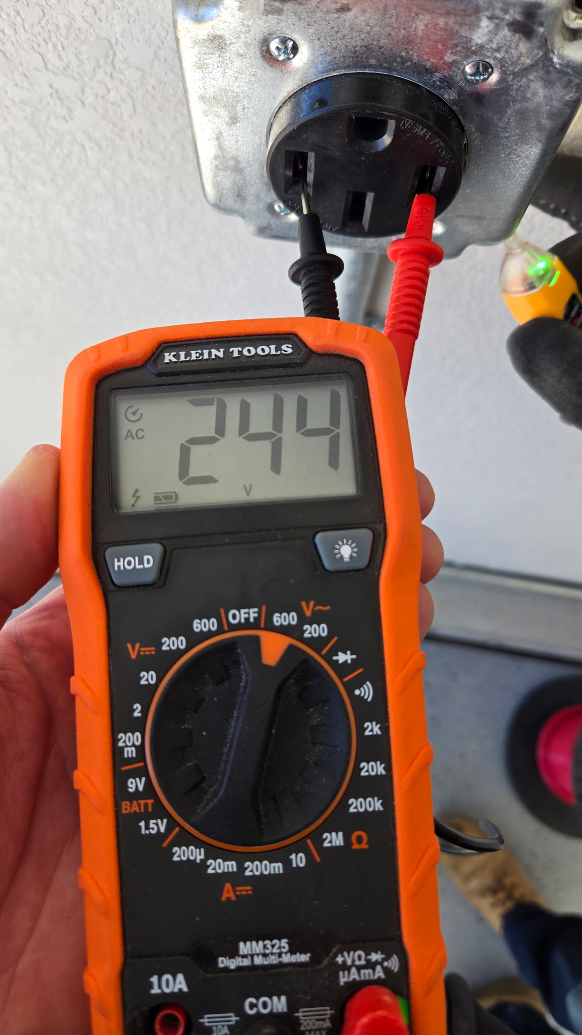 A digital multimeter displays a voltage reading of 249 volts AC while connected to an electrical outlet.