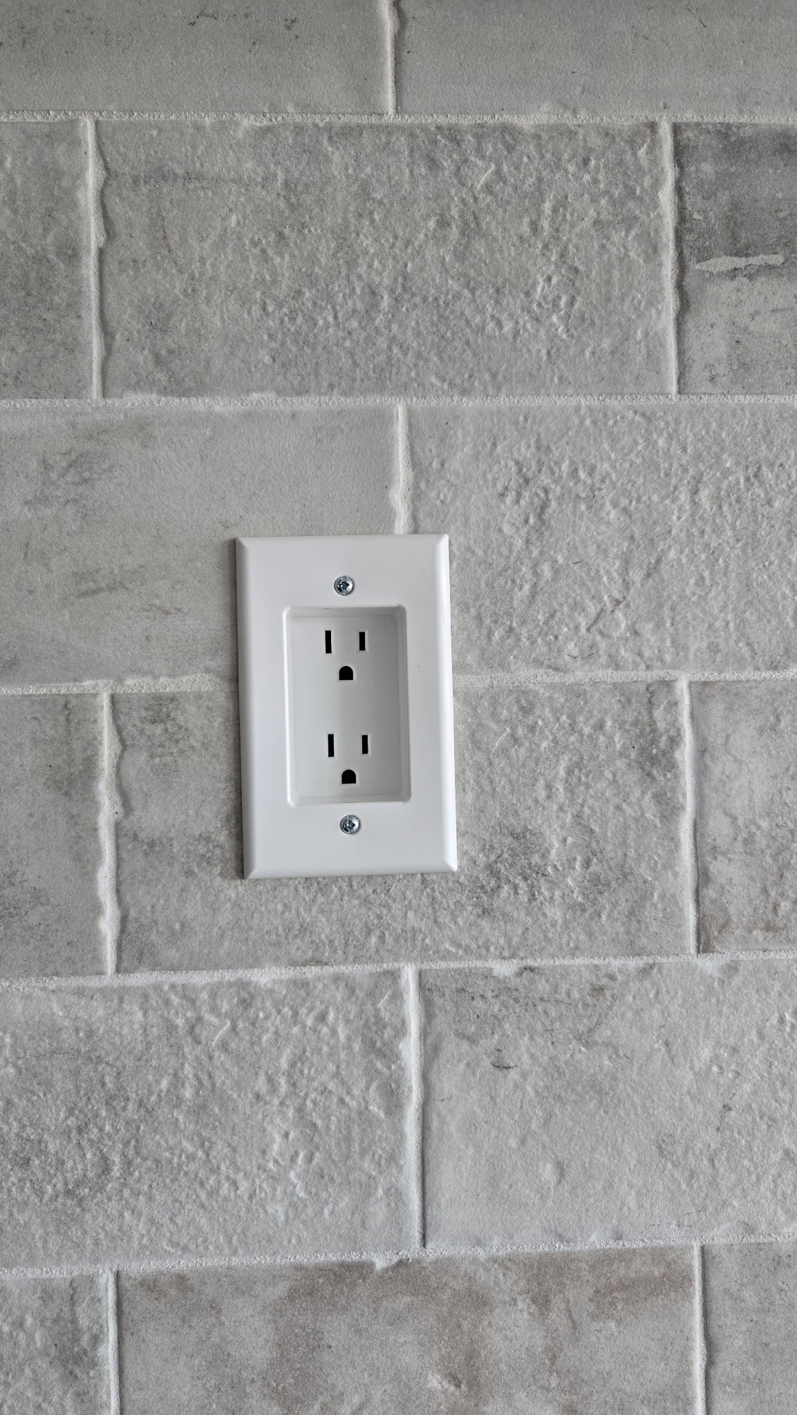 A white electrical outlet with two sockets is mounted on a gray textured tile wall, ideal for easy access or quick Outlet Not Working Repair.